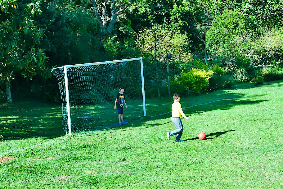 Crianças jogando futebol no grande gramado da Aldeia